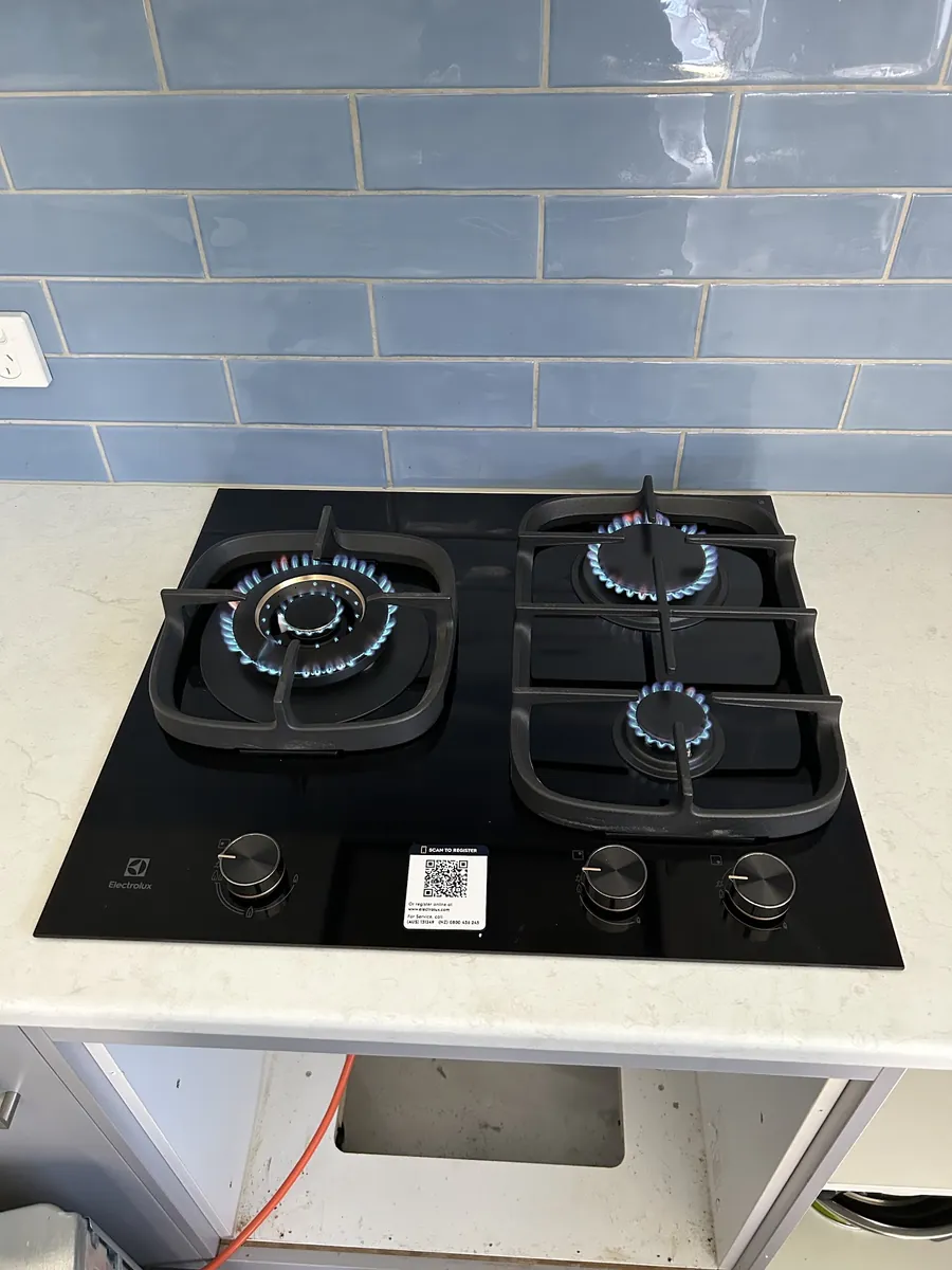 Black Electrolux gas cooktop with blue flames, freshly installed under a blue tiled splashback